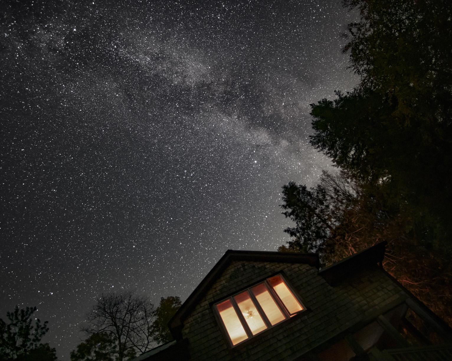 The Milky Way above a cabin with lights on